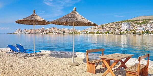 Peaceful beach with umbrellas, chairs, and a view of Saranda across the bay.