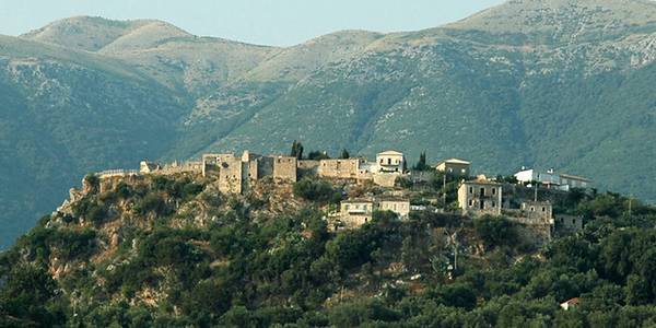 Old Himara village on a hill, surrounded by green mountains.