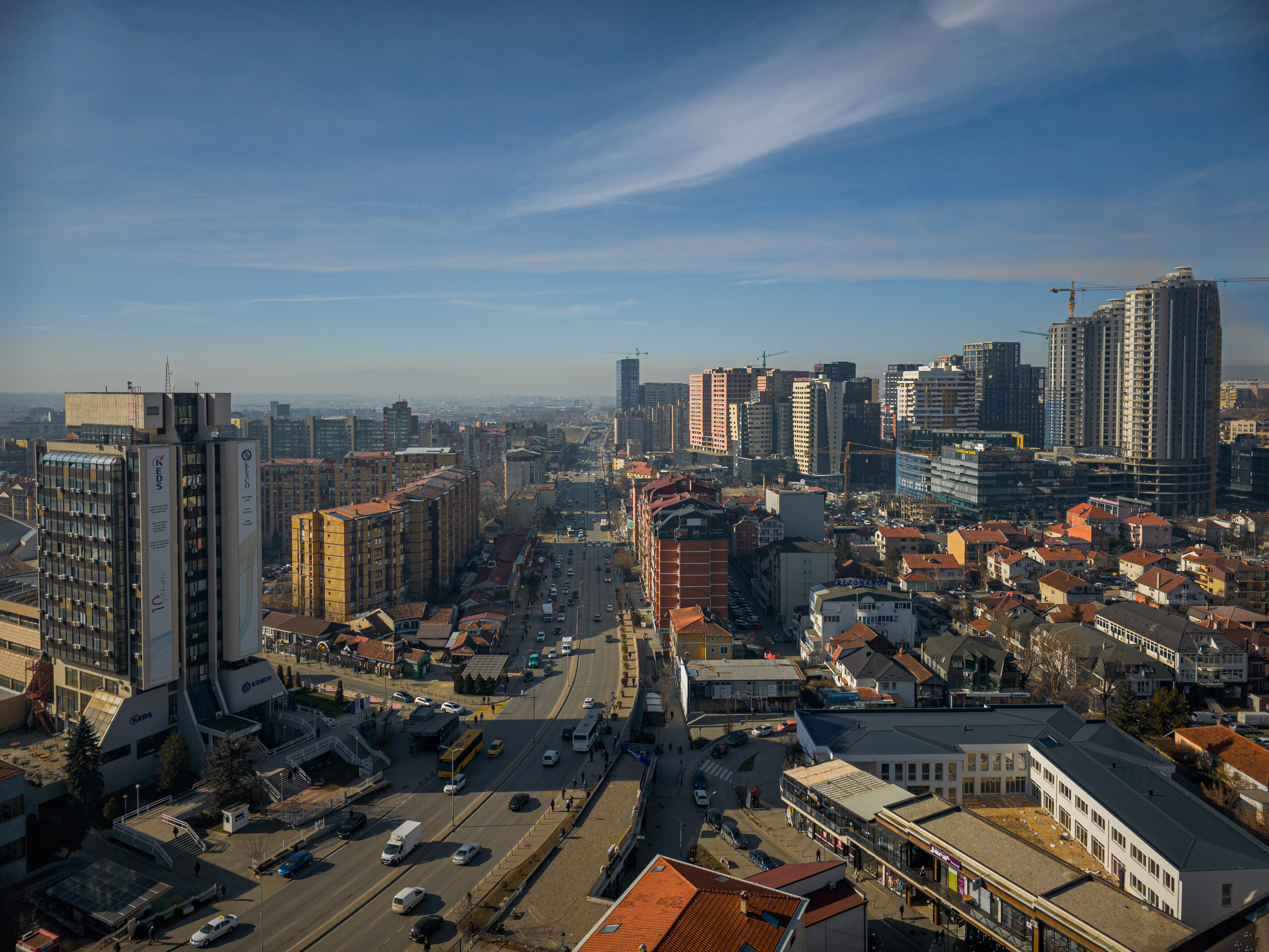 Një pamje dinamike e Prishtinës, që shfaq një kombinim të qiellgërvishtëseve moderne, ndërtesave të vjetra dhe rrugëve të zëna, duke pasqyruar rritjen e shpejtë të qytetit.