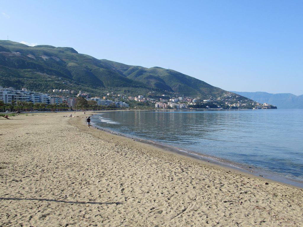 Një plazh i gjatë me rërë në Vlorë, me ujëra të qetë dhe pamje nga malet