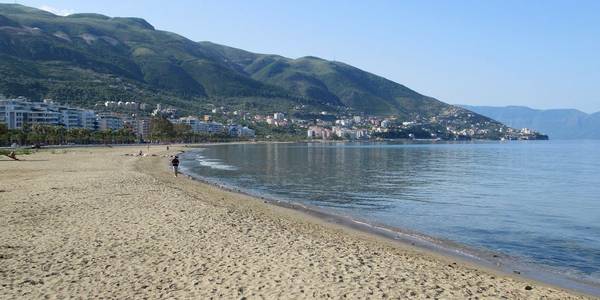 Një plazh i gjatë me rërë në Vlorë, me ujëra të qetë dhe pamje nga malet